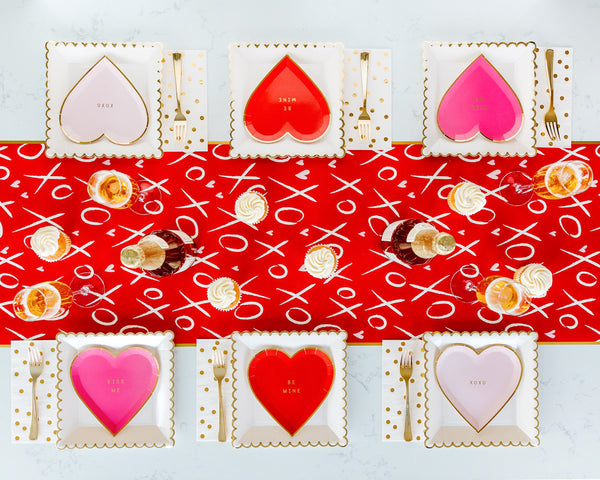 Red paper table runner with white XO and pink hearts. The perfect bottom layer to your Valentine's tablescape. By My Minds Eye, Available at A Little Confetti.